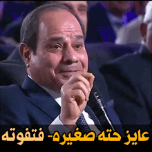 a man in a suit and tie is talking into a microphone with arabic writing behind him