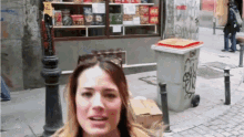 a woman is standing in front of a store with a trash can that says ' a ' on the lid