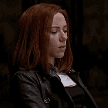 a woman with red hair is wearing a black leather jacket and looking at the camera .