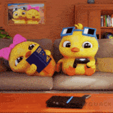two cartoon ducks are sitting on a couch one is reading a book and the other is playing a game