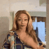 a woman in a blue and gold shirt is standing in a kitchen and making a funny face .