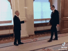 two men in suits are standing next to each other in a hallway with tiktok written on the bottom right