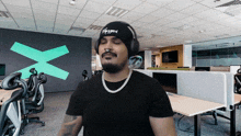 a man in an office wearing headphones and a beanie that says ' i 'm tired ' on it