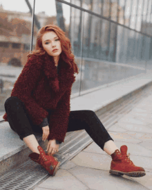 a woman wearing a red fur coat and red boots sits on a sidewalk