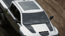 a white truck with a black hood is driving on a wooded road