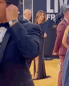 a man in a tuxedo is taking a picture of a woman in front of a sign that says live