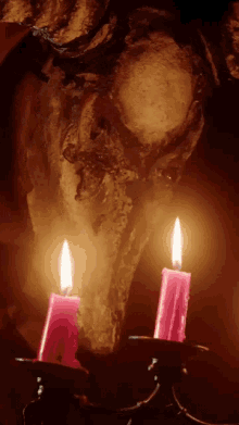 two red candles are lit in front of a skull