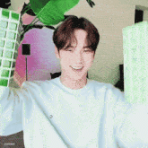 a young man in a white sweater is smiling and holding a green plant