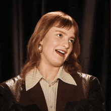 a woman wearing a striped shirt and a black jacket smiles