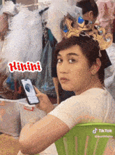 a man with a crown on his head is holding a cell phone with a sticker that says hihihi on it