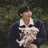 a man in a purple jacket is holding two small white puppies