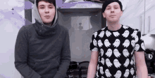 two men are standing next to each other in a kitchen . one of the men is wearing a ghost shirt .