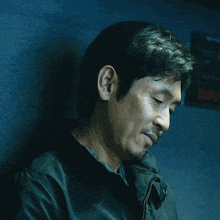 a man in a black jacket is leaning against a wall and looking at the camera