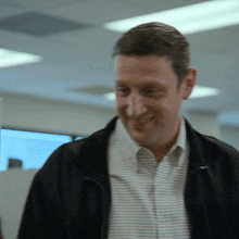 a man wearing a striped shirt and a black jacket is smiling