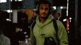 a man wearing headphones and a green hoodie is walking through a crowded room .