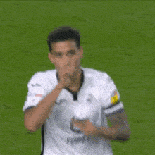 a soccer player in a white jersey is blowing a kiss on a soccer field .