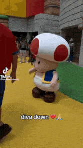 a toad mascot is standing on a yellow floor next to a person .
