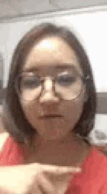 a woman wearing glasses and a red shirt is pointing her finger at the camera .