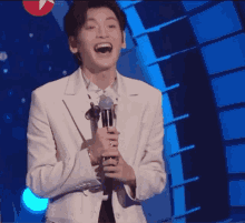 a man in a white suit is holding a microphone and laughing on stage .