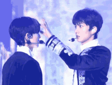 two men are touching each other 's faces with their hands while wearing a microphone .