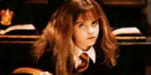 hermione granger from harry potter is sitting at a desk in a classroom with a book .