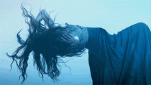 a woman in a blue dress is laying down with her hair flying in the wind