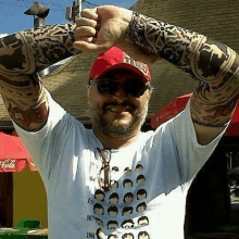 a man with tattoos on his arms is wearing a hat , sunglasses and a t-shirt .