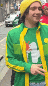 a man wearing a green and yellow jacket and a yellow beanie has a gifrun.com watermark on the bottom right