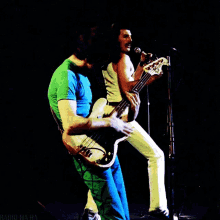 a man in a green shirt is playing a bass guitar next to a man in white pants
