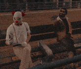 a man in a clown mask sits next to another man on a bench that has the letter b on it