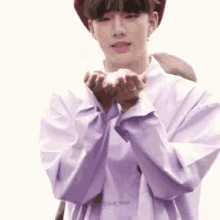 a young man wearing a purple shirt and a red hat is holding a heart in his hands .
