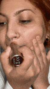 a woman with a nose ring is applying lipstick on her face