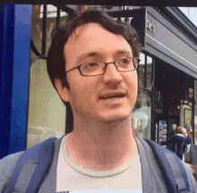 a man wearing glasses stands in front of a store that says ' the ' on the sign