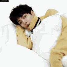 a young man wearing a yellow sweater is laying on a bed with a blanket that says crown goose
