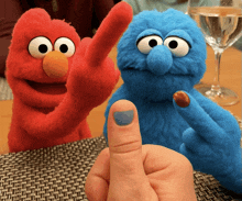 elmo and cookie monster are on a table with a person 's finger in front of them