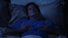 a man in a blue shirt is laying in bed holding his chest
