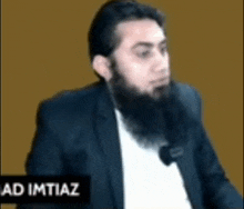 a man with a beard is wearing a suit and headphones while talking into a microphone .
