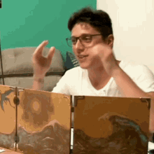 a man wearing glasses and a white shirt is sitting at a table with a painting on it