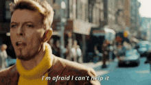 a man in a yellow sweater says i 'm afraid i can 't help it while walking down a street
