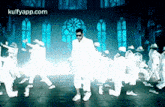 a man in a white suit is dancing with a group of dancers in a dark room .