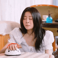 a woman is sitting at a table with her eyes closed while holding a vacuum cleaner .