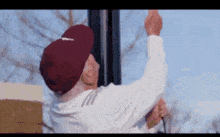 an elderly man wearing a maroon hat and a white shirt is hanging a light pole .