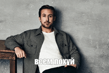 a man in a plaid jacket sits next to a wooden table with the words " всем похуй " written below him