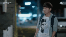 a young man with a backpack is standing in front of a building at night .
