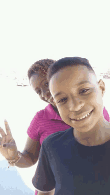 a woman in a pink shirt is standing next to a boy in a black shirt who is giving a peace sign .