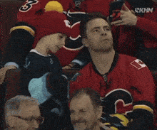 a boy wearing a red hat with the number 3 on it sits next to a man in a red jersey