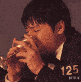 a man is drinking from a glass with the number 125 on his shirt