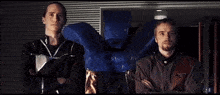 two men standing next to each other with one holding a blue bag that says ' i 'm sorry '