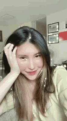 a woman with long black hair is holding her hand to her forehead and smiling .
