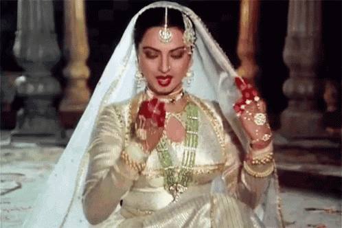 a woman in a white dress and veil is holding red flowers .